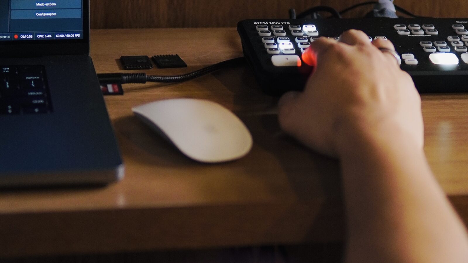 Mão operando um switcher de vídeo, com medidores de áudio na tela